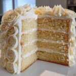 A slice cut from a stunning white rose cake reveals four layers of yellow sponge and white frosting.
