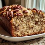 A moist slice of sweet alabama pecan bread, topped with whole pecans, resting on a white plate.