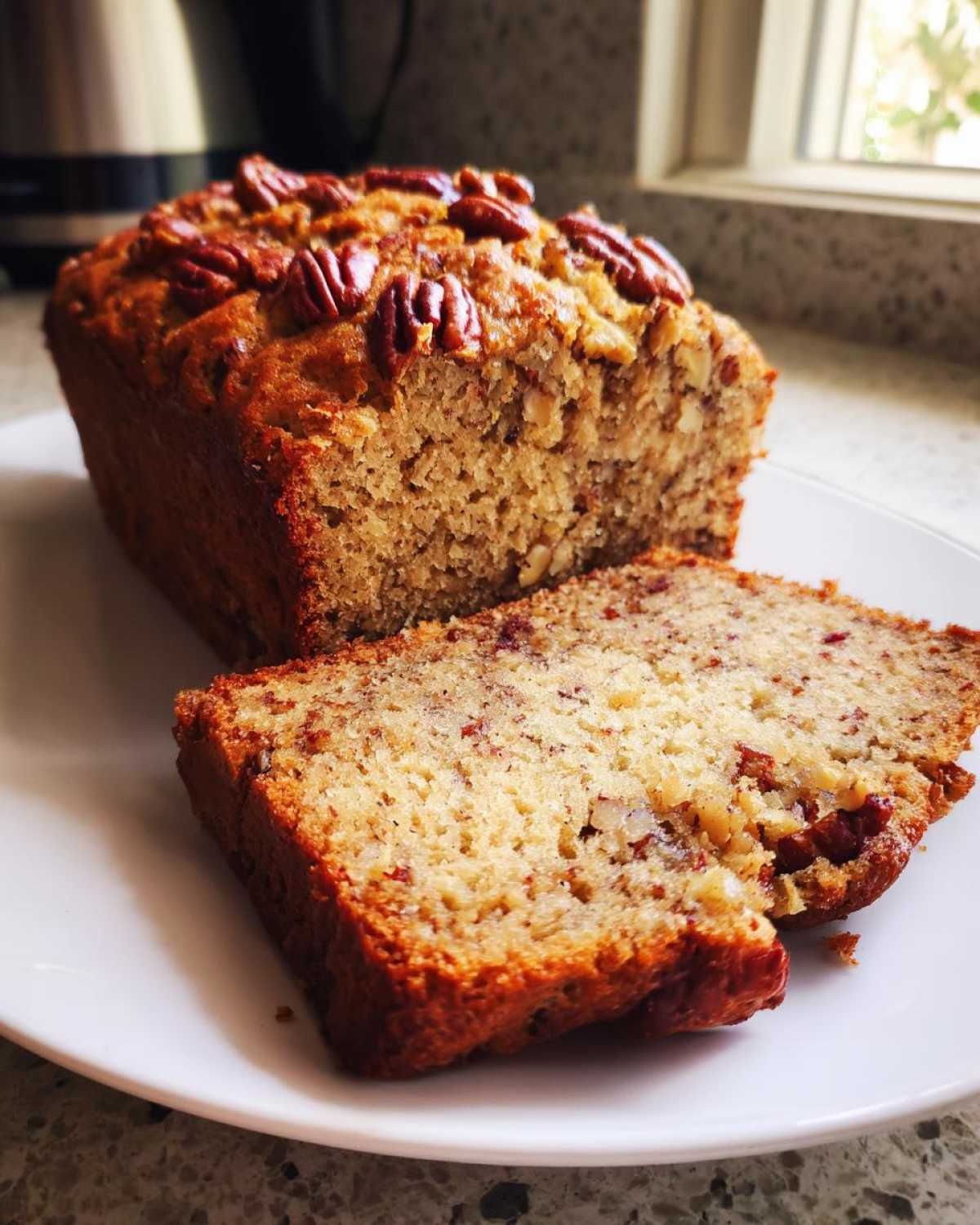 A close-up of a sliced loaf of Sweet Alabama Pecan Bread topped with whole pecans.