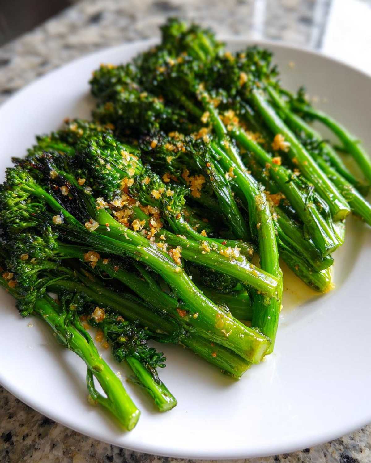 A plate of vibrant green, tender broccolini stalks seasoned with golden breadcrumbs or garlic.