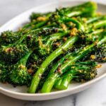 Close-up of bright green, roasted broccolini tossed with crispy garlic bits served on a white platter.
