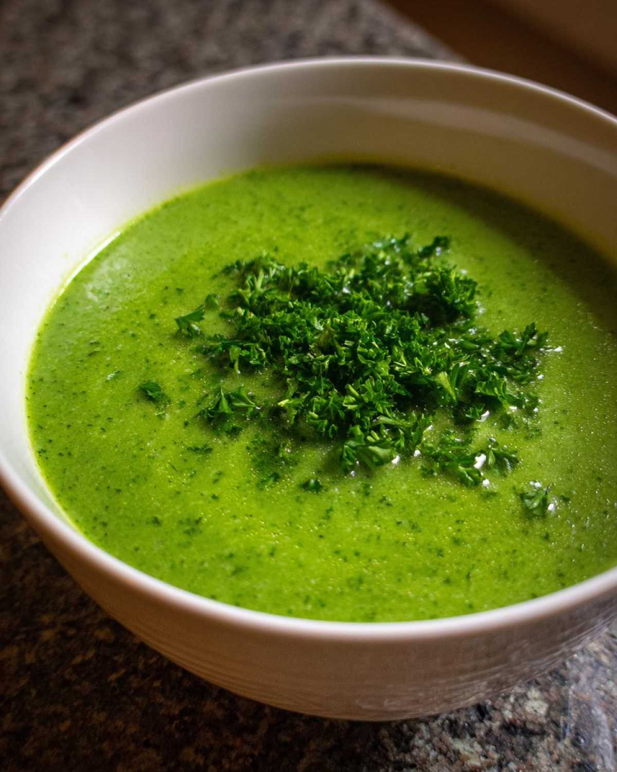 Close-up of a bowl of bright green zucchini soup topped with fresh chopped parsley.