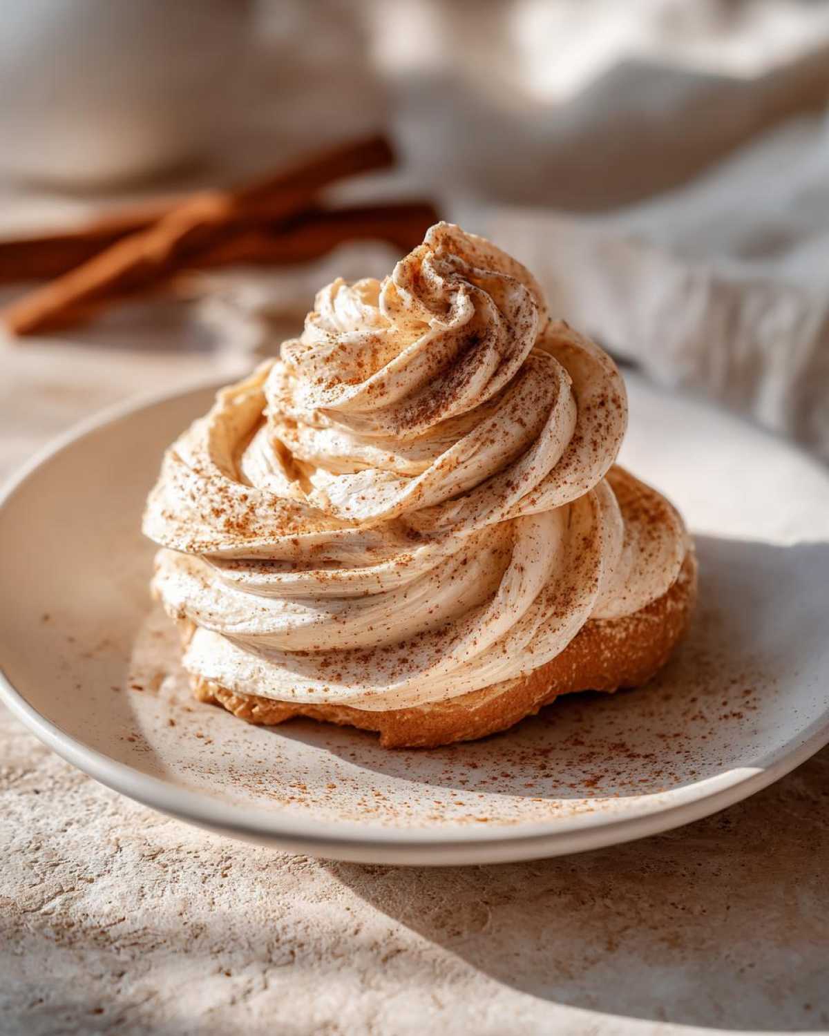 A swirl of decadent cinnamon butter topping dusted with cinnamon on a biscuit, with cinnamon sticks blurred in the background.