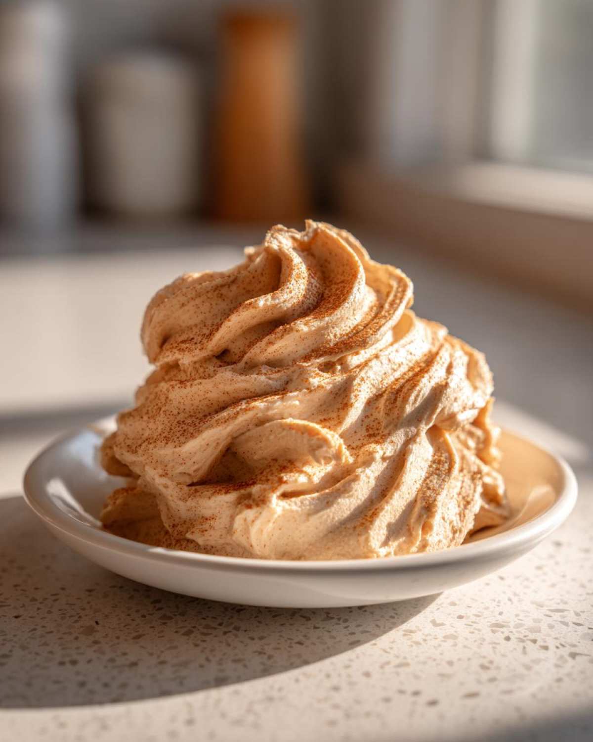 A beautiful swirl of whipped cinnamon butter, dusted with extra spice, served on a small white dish.