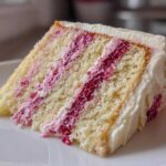 A close-up of a moist slice of white chocolate raspberry cake with layers of white cake and bright pink raspberry filling.
