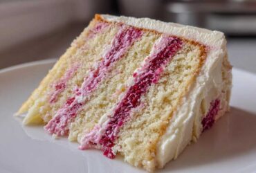 A close-up of a moist slice of white chocolate raspberry cake with layers of white cake and bright pink raspberry filling.