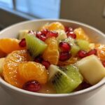 Close-up of a vibrant winter fruit salad featuring mandarin oranges, kiwi slices, and pomegranate seeds in a white bowl.