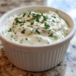 A close-up of creamy 5-Minute Greek Yogurt Ranch Dip topped with fresh chopped parsley in a white fluted ramekin.