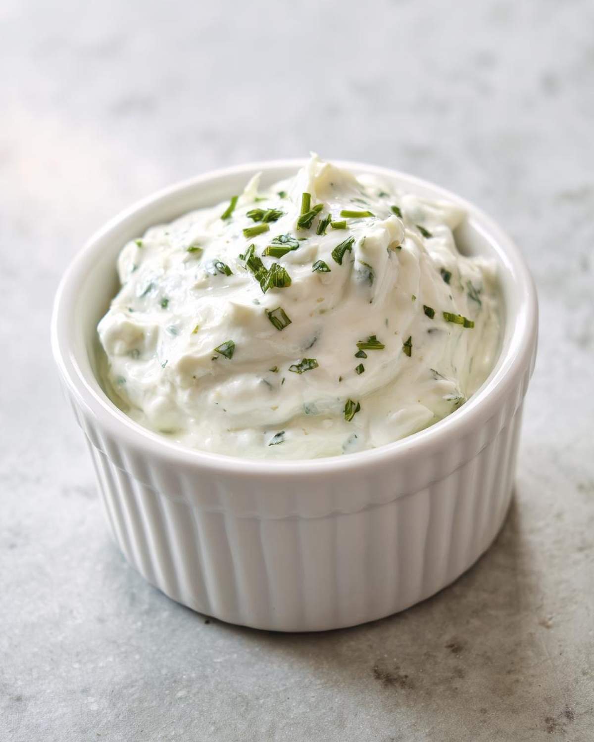 A close-up of creamy 5-Minute Greek Yogurt Ranch Dip topped with fresh chopped chives in a white ramekin.