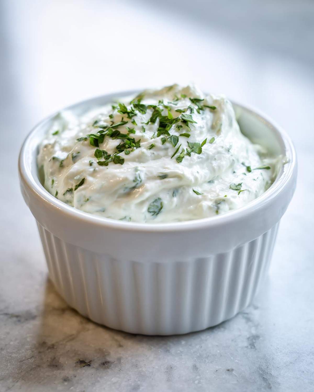 A close-up of creamy 5-Minute Greek Yogurt Ranch Dip topped with fresh chopped parsley in a white ramekin.