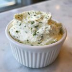 Close-up of thick, creamy 5-Minute Greek Yogurt Ranch Dip topped with fresh green herbs in a white ramekin.