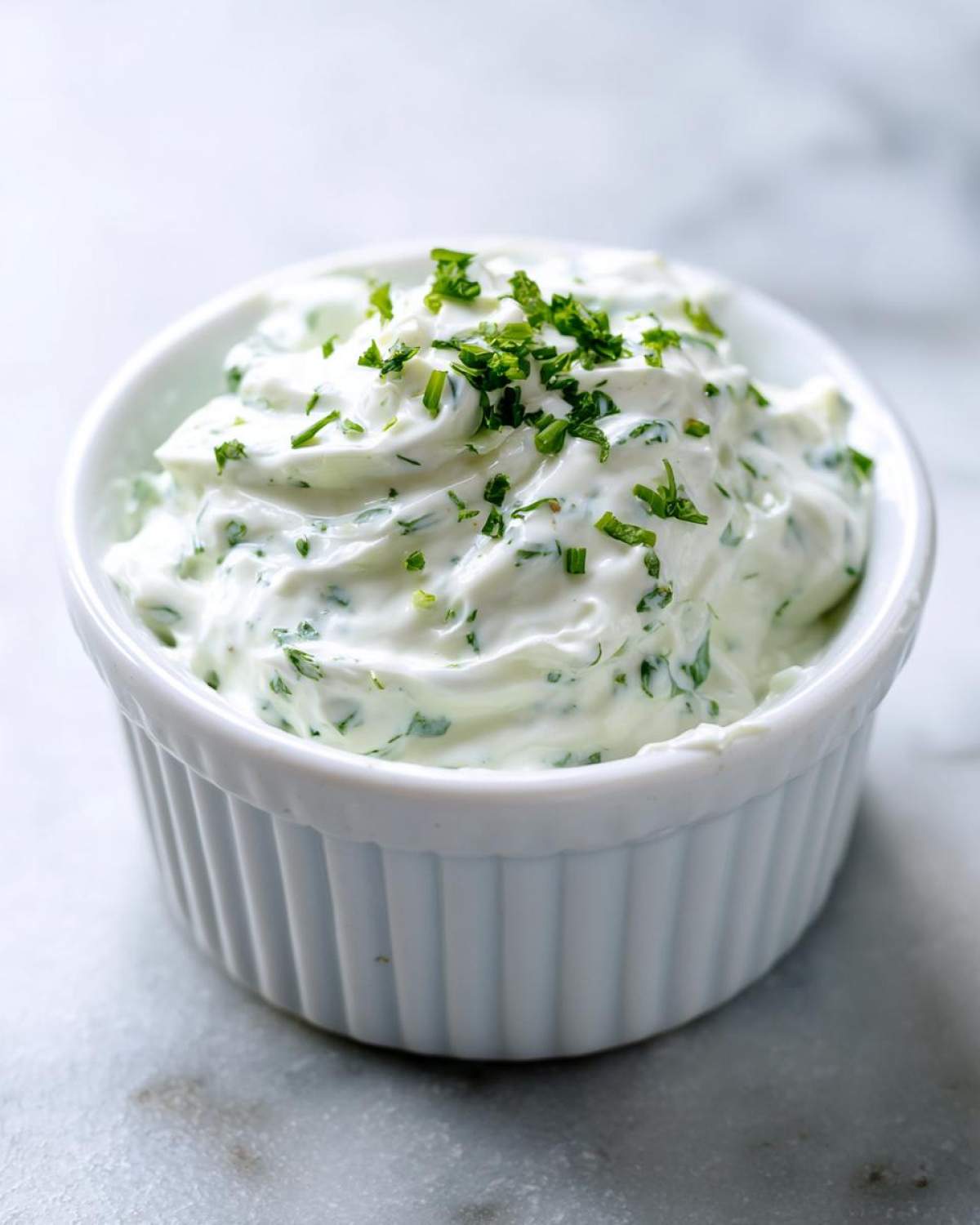 A close-up shot of creamy 5-Minute Greek Yogurt Ranch Dip, topped with fresh chopped herbs, served in a white fluted ramekin.