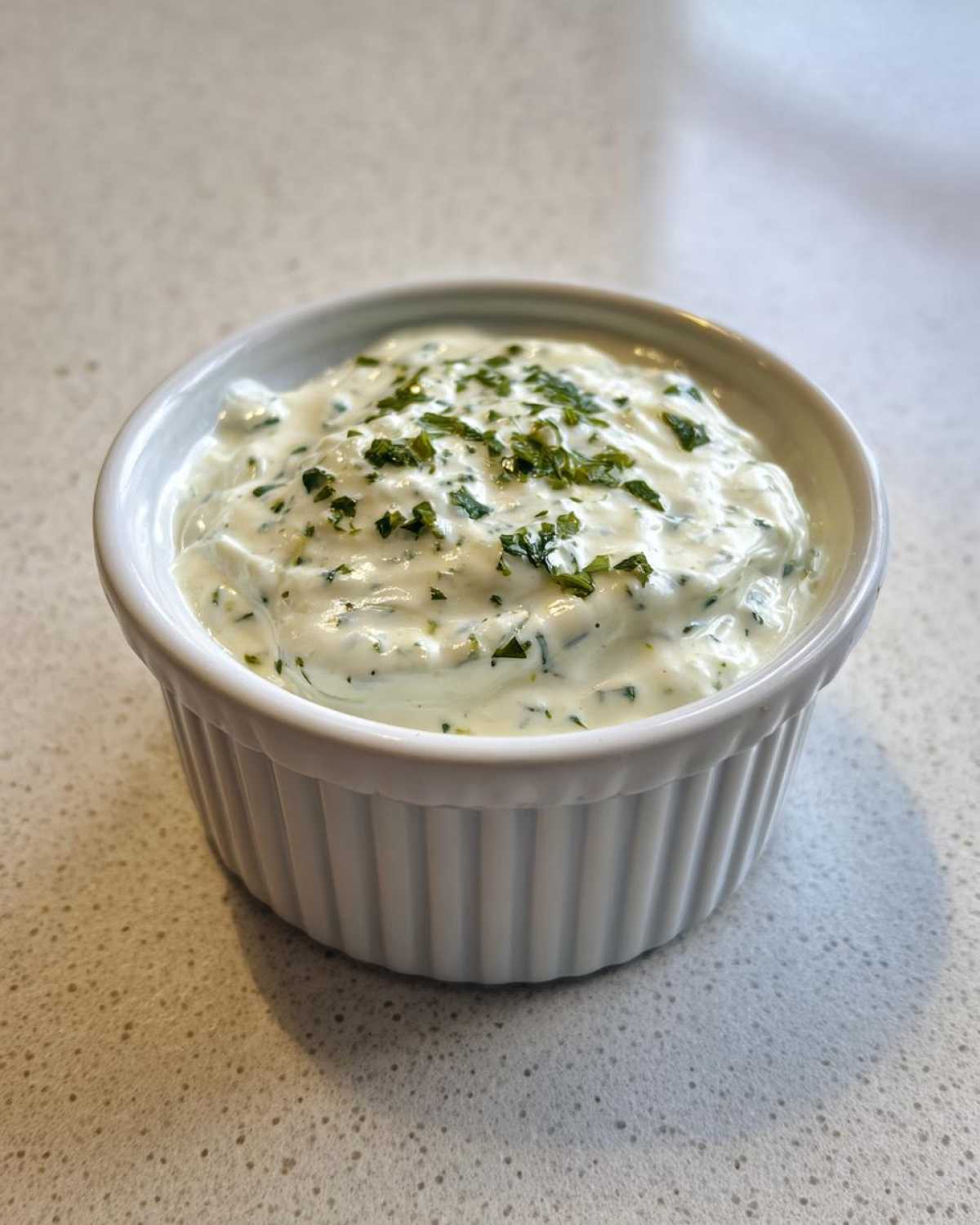 A small white ramekin filled with creamy 5-Minute Greek Yogurt Ranch Dip, topped with fresh parsley.