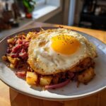 A plate of crispy Air Fryer Corned Beef Hash topped with a perfectly cooked sunny-side-up egg seasoned with pepper.