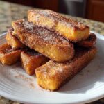 A stack of golden brown Air Fryer French Toast Sticks generously coated in cinnamon sugar on a white plate.