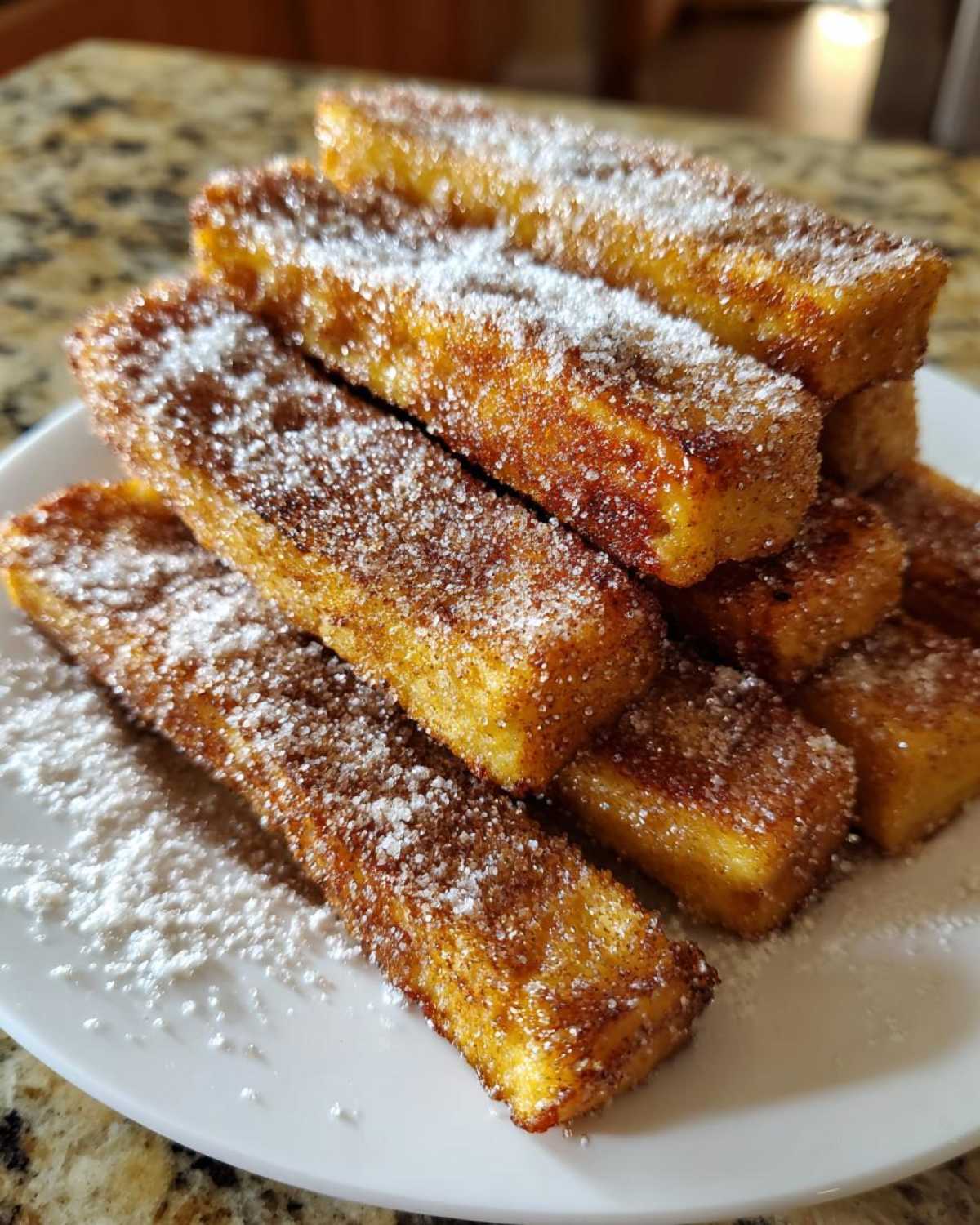 A stack of golden brown Air Fryer French Toast Sticks generously coated in cinnamon sugar and powdered sugar.