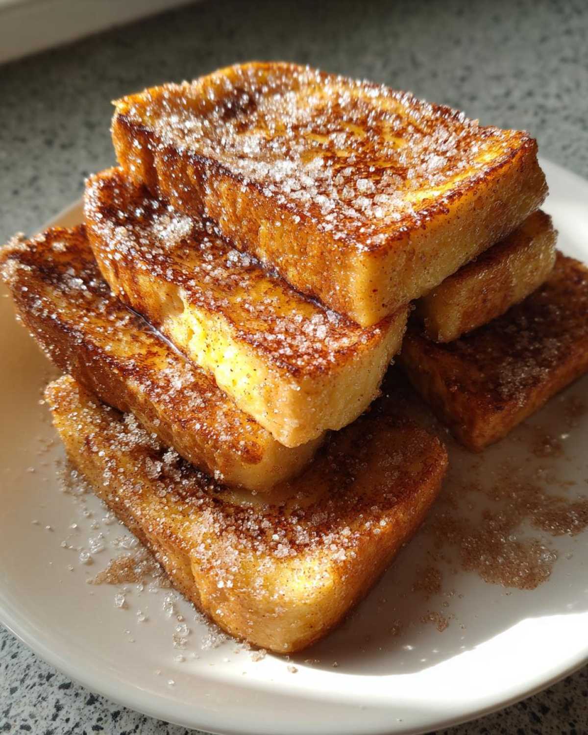 Close-up of thick Air Fryer French Toast Sticks stacked on a white plate, heavily coated in cinnamon sugar.