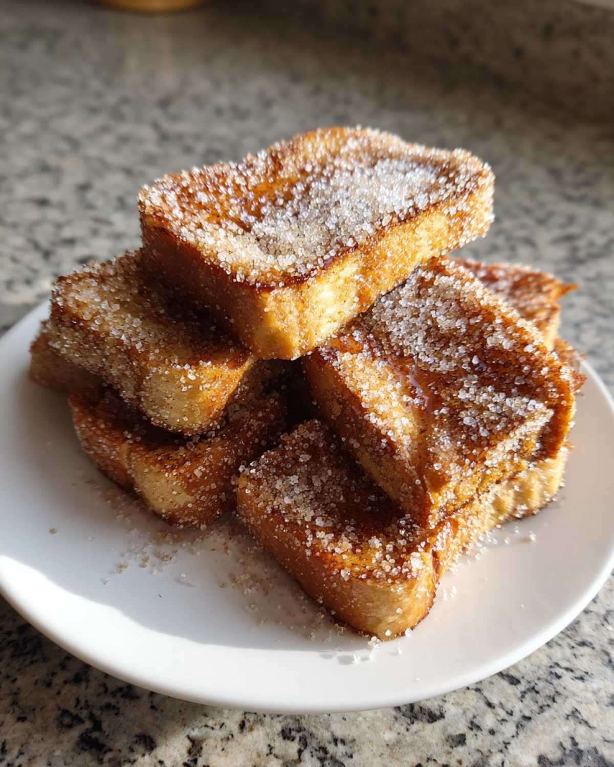 A stack of golden brown Air Fryer French Toast Sticks heavily coated in cinnamon sugar on a white plate.