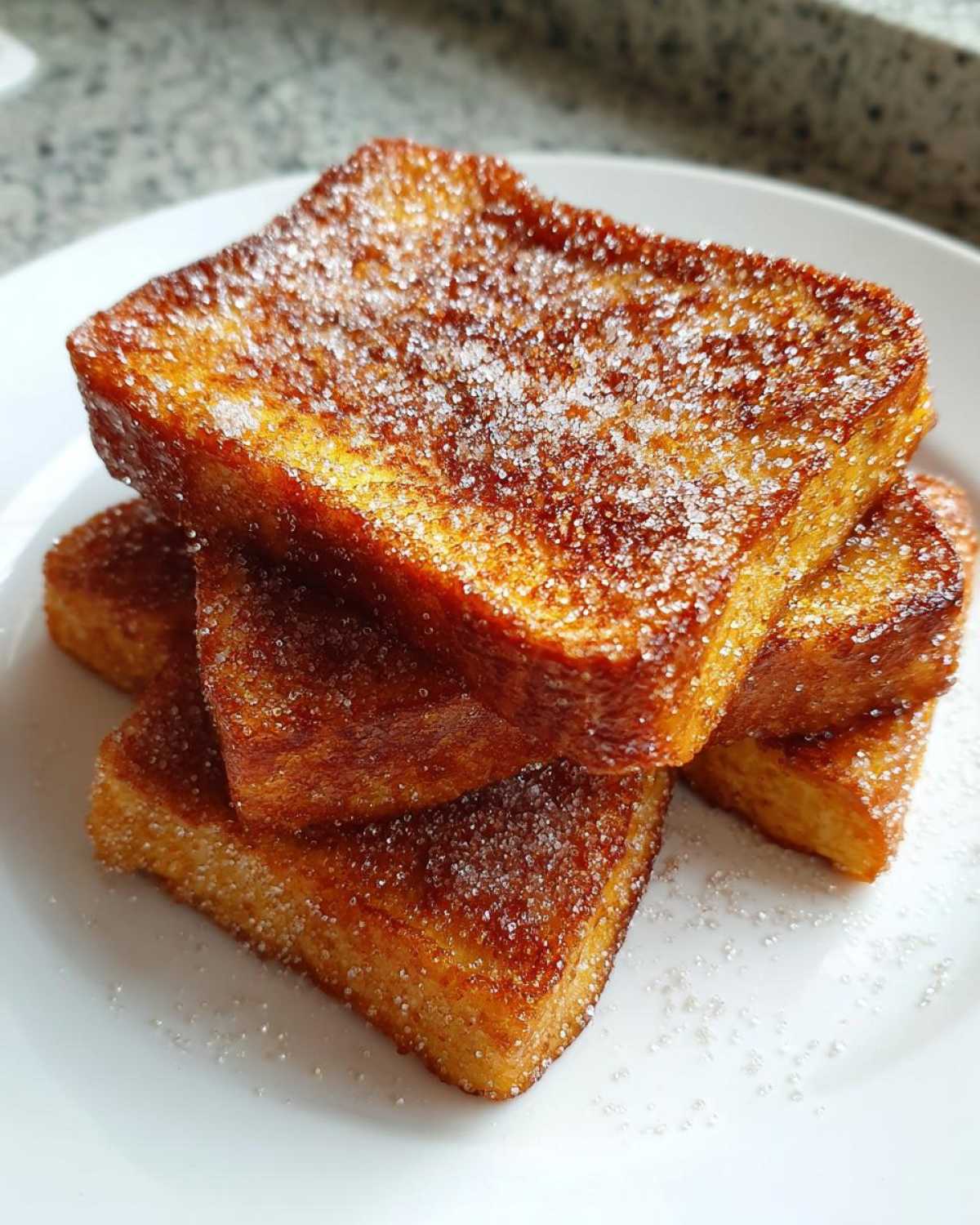 A stack of golden brown Air Fryer French Toast Sticks generously coated in sparkling cinnamon sugar.