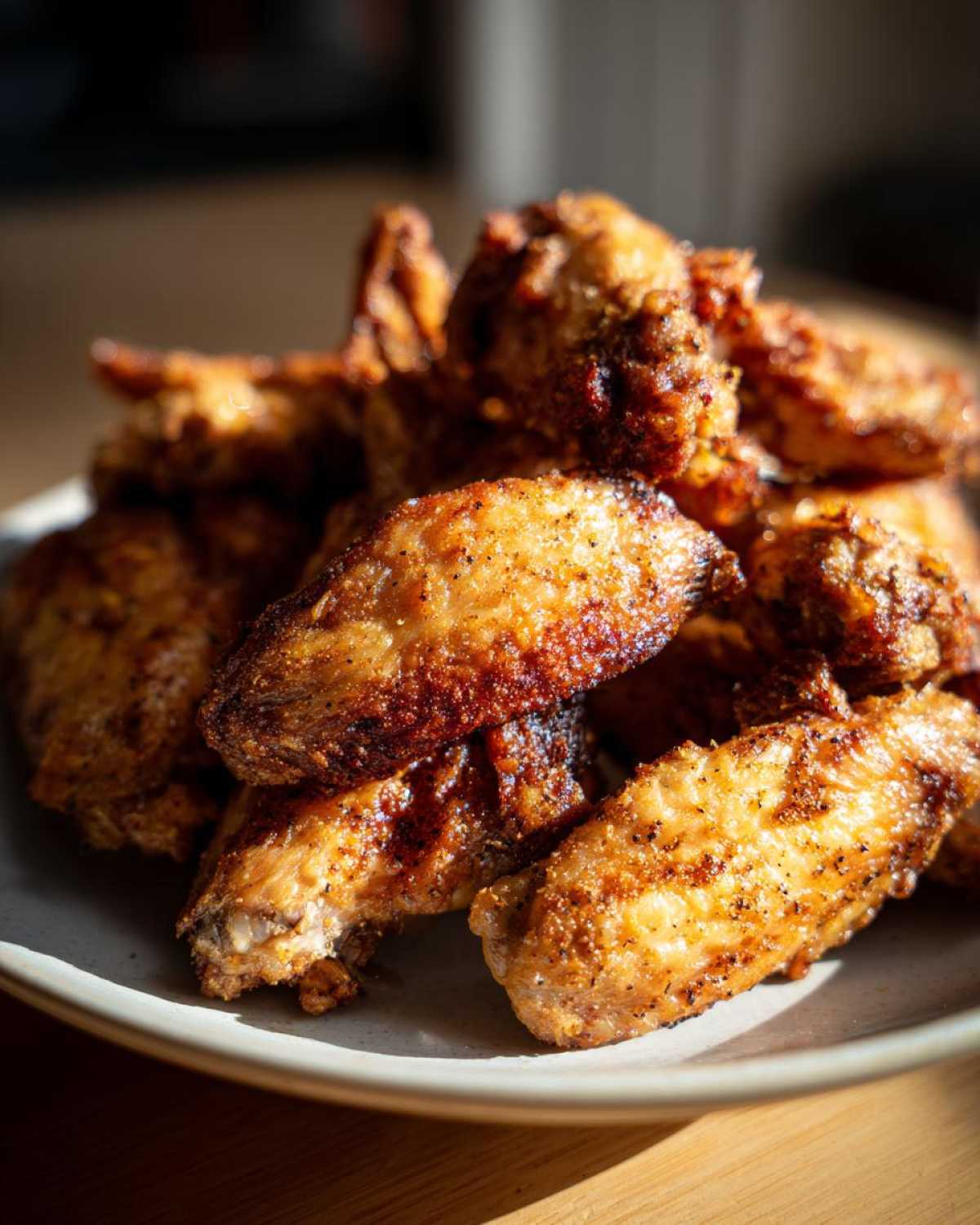 A close-up of a pile of crispy, golden-brown Air Fryer Lemon Pepper Wings seasoned with visible black pepper.