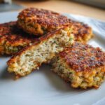 Close-up of Air Fryer Salmon Patties, one cut in half showing the flaky interior texture and herbs.