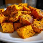 A close-up of golden brown, seasoned Air Fryer Sweet Potato Cubes piled on a white plate.