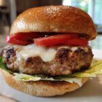 Close-up of a juicy Air Fryer Turkey Burger topped with melted white cheese and fresh tomato slices on a toasted bun.
