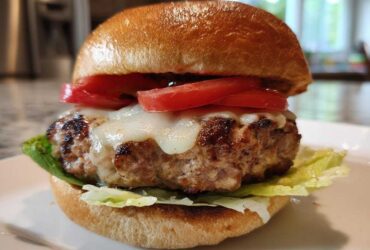 Close-up of a juicy Air Fryer Turkey Burger topped with melted white cheese and fresh tomato slices on a toasted bun.