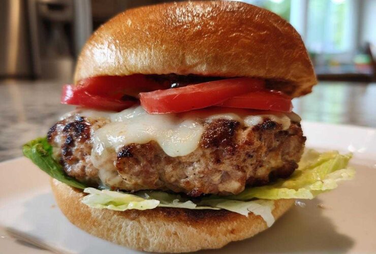 Close-up of a juicy Air Fryer Turkey Burger topped with melted white cheese and fresh tomato slices on a toasted bun.