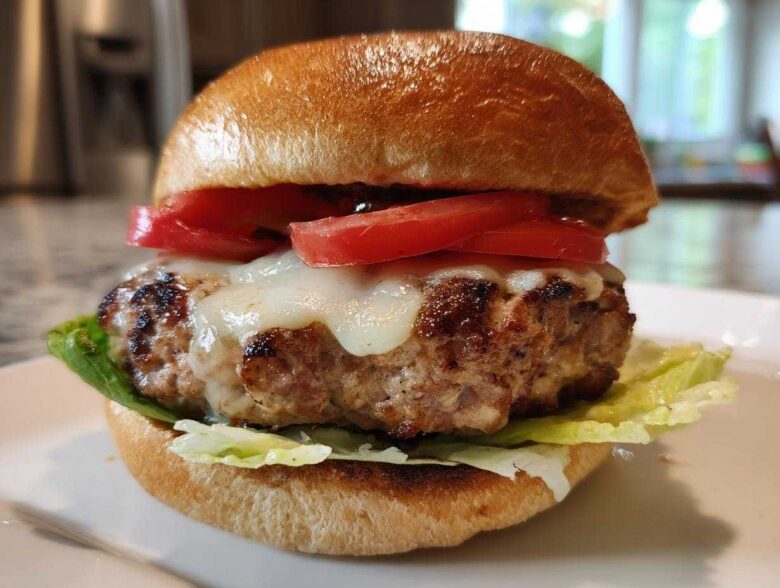 Close-up of a juicy Air Fryer Turkey Burger topped with melted white cheese and fresh tomato slices on a toasted bun.