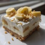 A single serving of Banana Pudding Cheesecake Bars topped with whipped cream, banana slices, and crumbs.