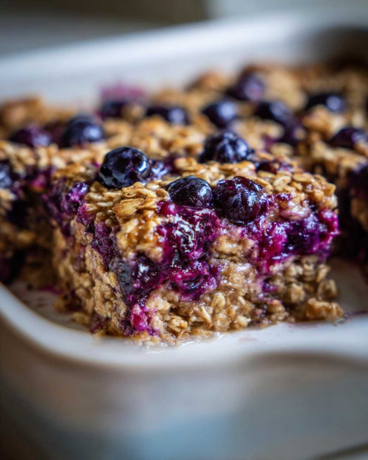 A close-up, macro shot of a moist square of Blueberry Baked Oatmeal Squares showing oats and bursting blueberries.