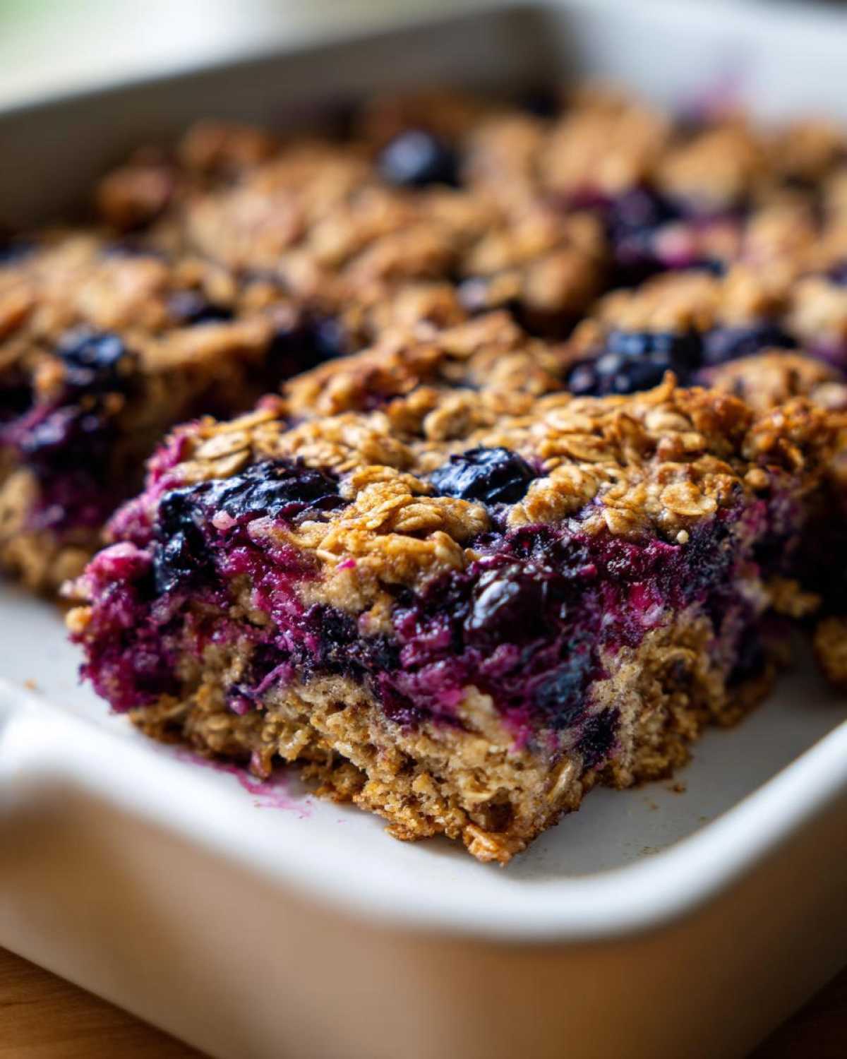 A close-up view of a freshly baked square of Blueberry Baked Oatmeal Squares showing the moist, purple blueberry filling and oat topping.