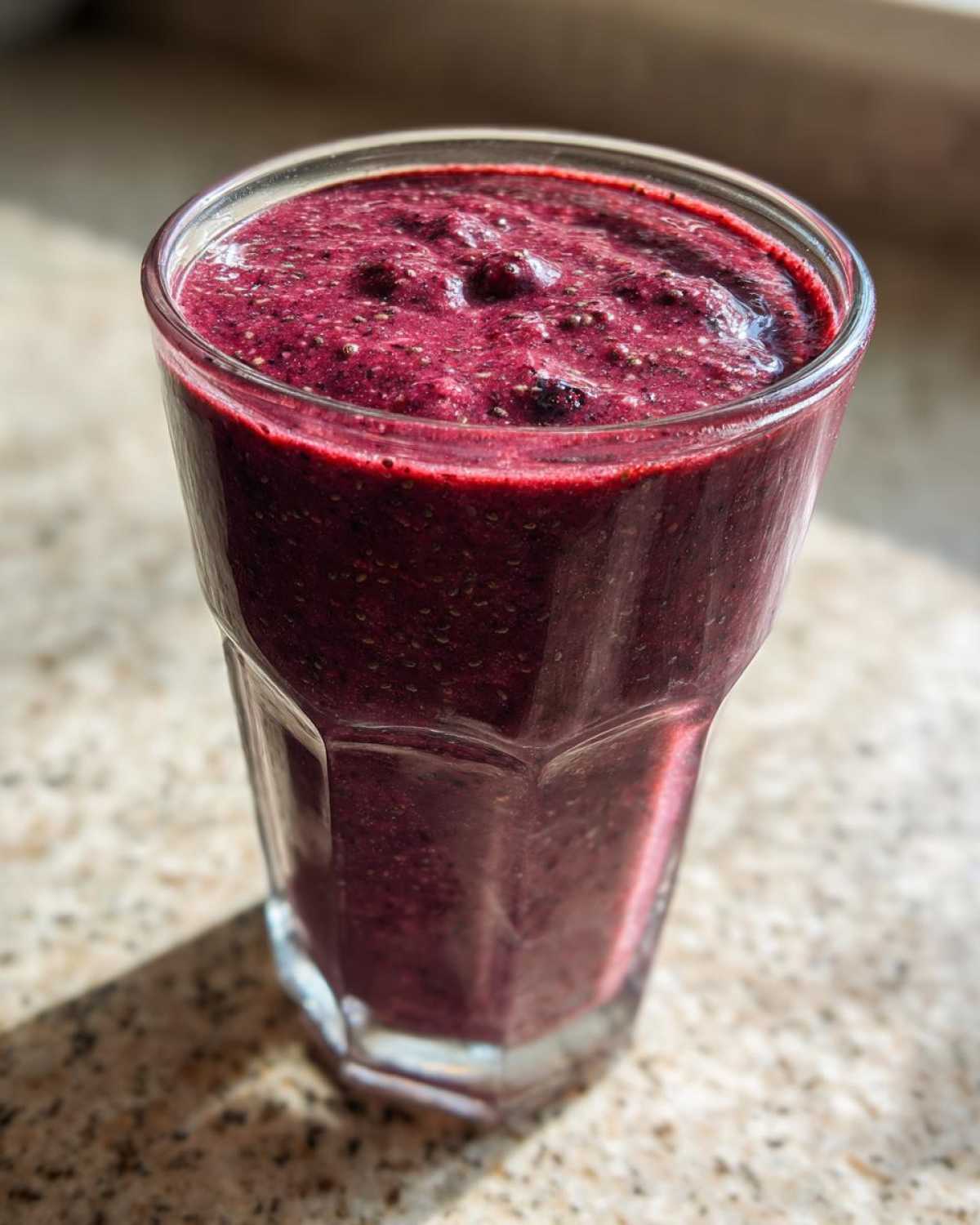 A close-up of a thick, deep purple Blueberry Lemon Chia Smoothie in a faceted glass, showing visible chia seeds.