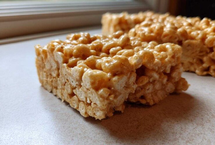 Two thick, chewy squares of Brown Butter Rice Krispie Treat Bars sitting on a light countertop near a window.