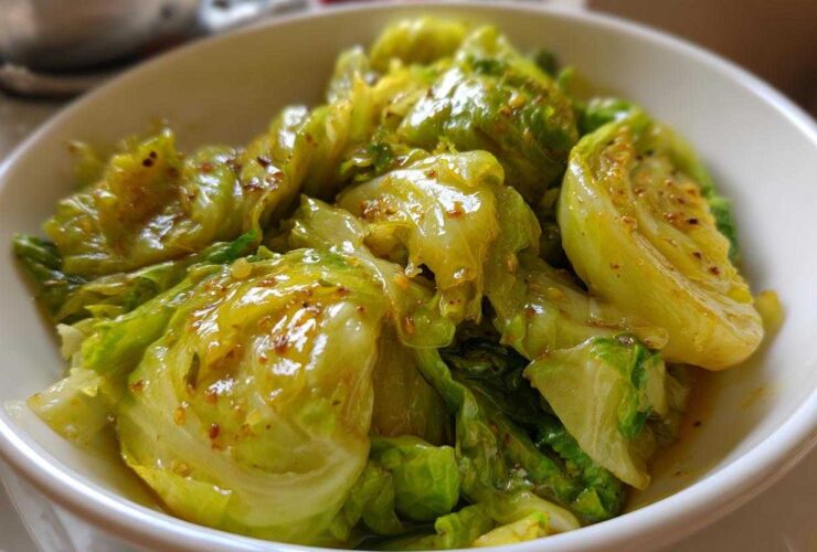 Close-up of glossy, bright green cabbage pieces coated in a savory Garlic Ginger Sauce in a white bowl.