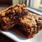 Two thick, gooey Chewy Chocolate Chip Cookie Bars sitting on a white plate, showing melted chocolate centers.
