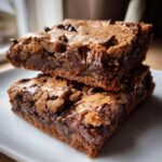 Two rich, fudgy Chewy Chocolate Chip Cookie Bars stacked on a white plate, showing melted chocolate chips.