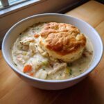A bowl of creamy Chicken Pot Pie Soup topped with a golden, fluffy biscuit.