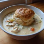 A bowl of creamy Chicken Pot Pie Soup topped with a golden, flaky biscuit.