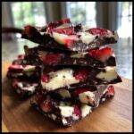 A stack of four pieces of Chocolate Covered Strawberry Bark featuring dark chocolate, white chocolate swirls, and bright red strawberries.