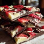 A stack of broken pieces of Chocolate Covered Strawberry Bark featuring dark chocolate, white chocolate swirls, and fresh strawberry slices.
