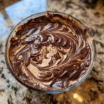 Overhead view of rich Chocolate Peanut Butter Cheesecake Dip swirled with dark chocolate in a clear glass bowl.