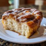 A close-up of a single serving of Cinnamon Roll Overnight French Toast Bake, drizzled with white icing.