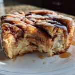 Close-up of a serving of Cinnamon Roll Overnight French Toast Bake, drizzled with white icing and syrup.