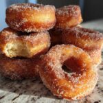 A stack of golden brown Cinnamon Sugar Air Fryer Donuts heavily coated in sparkling cinnamon sugar, one has a bite missing.