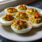 Six halves of Classic Deviled Eggs with Dill Pickle Relish, topped with paprika, arranged on a white plate.