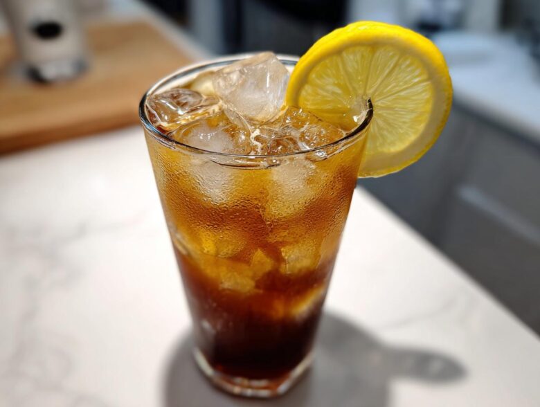 A tall glass filled with iced Cold Brew Lemonade, showing condensation and garnished with a bright lemon slice.