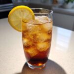 A tall glass filled with ice and dark brown Cold Brew Lemonade, garnished with a lemon wheel.