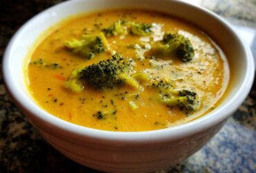 Close-up of a creamy, orange-yellow bowl of Copycat Broccoli Cheddar Soup with visible florets.
